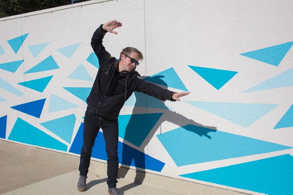 Brennen Bechtol “swims” beside the mural he painted for the pool. Photo by Macks Prewitt/The Et Cetera