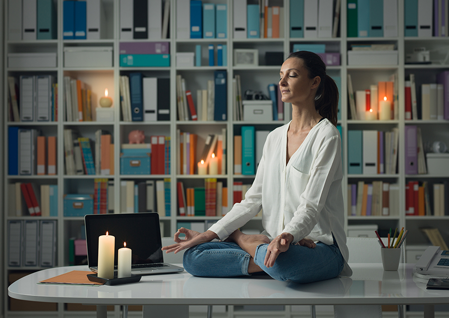 Relaxed woman practicing meditation at home at night, she is sitting in the lotus position on the office desk